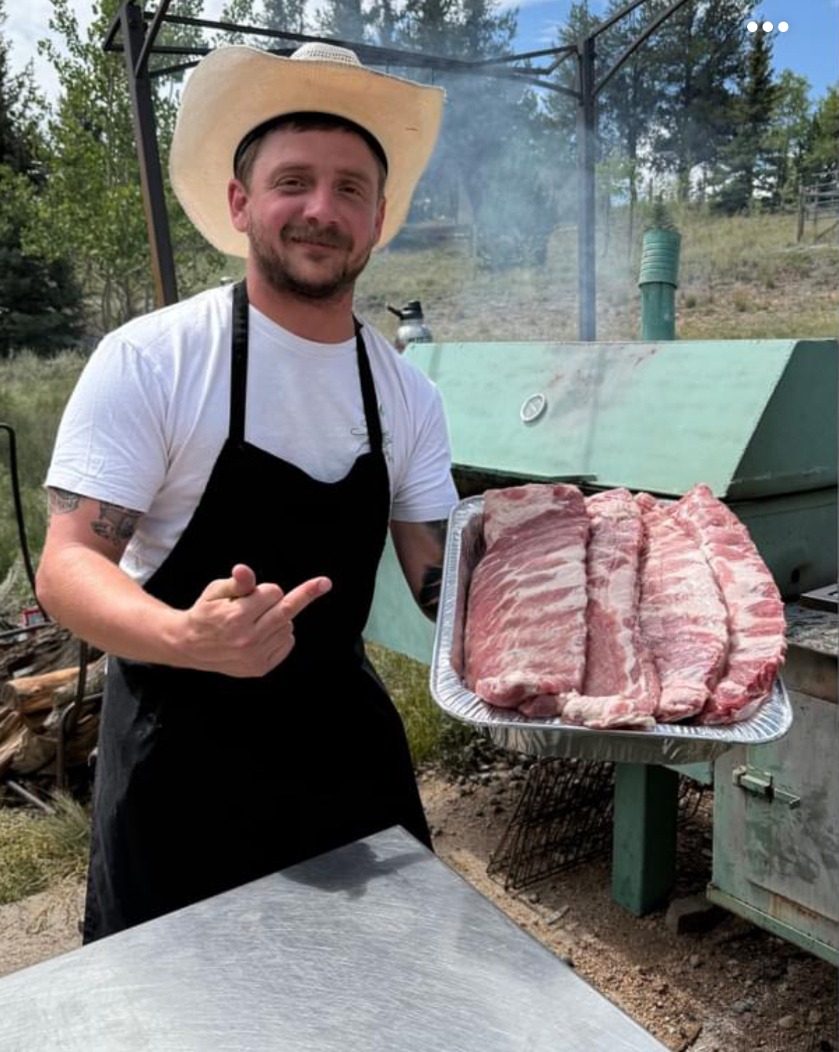 Stephen of Big Nasty BBQ holding a tray of pork ribs beside his offset smoker in Colorado